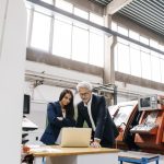 Businessman an woman in high tech enterprise, having a meeting, using laptop